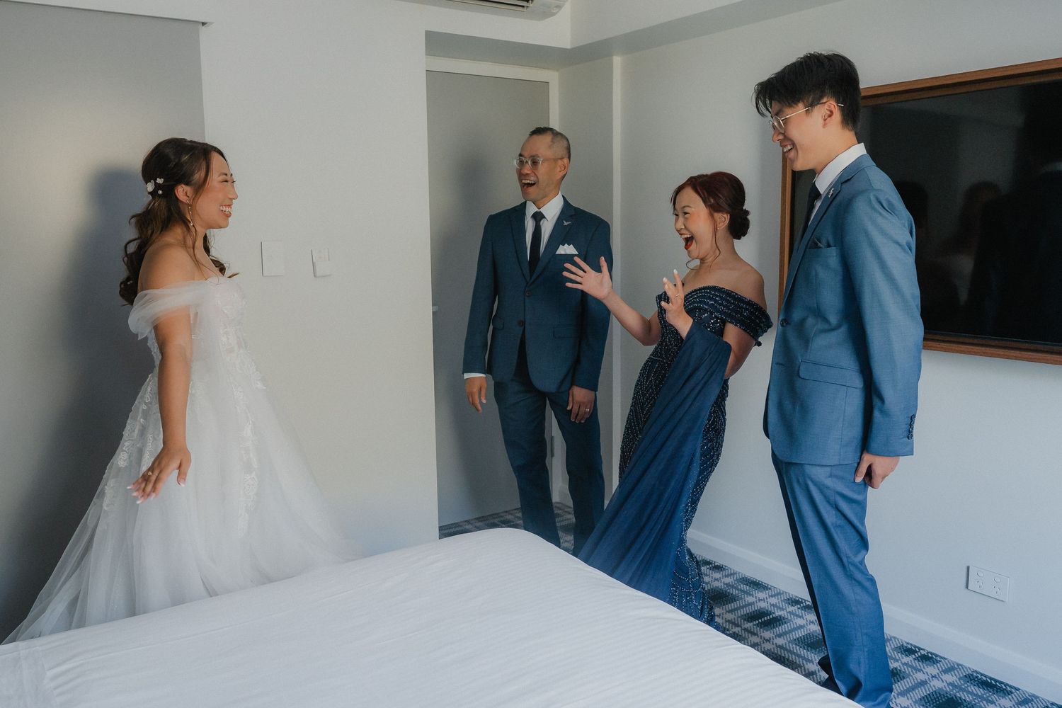 Wedding party sharing emotional reactions during first look photos in minimalist white room.