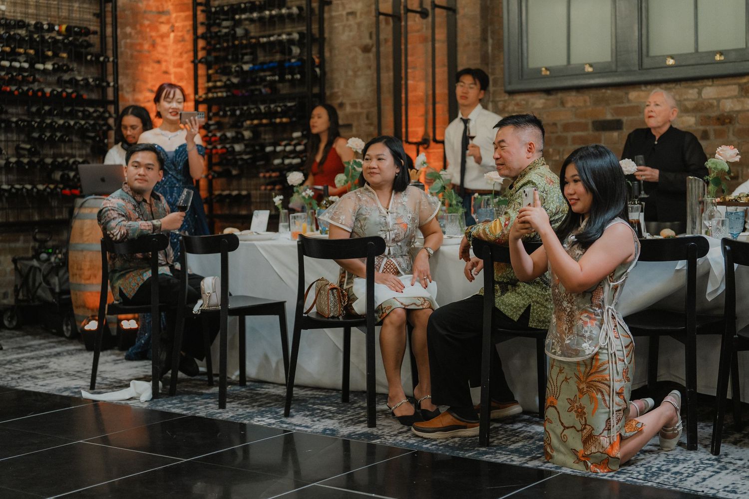 People enjoying a lively celebration at a rustic venue with wine racks and exposed brick walls in the background.