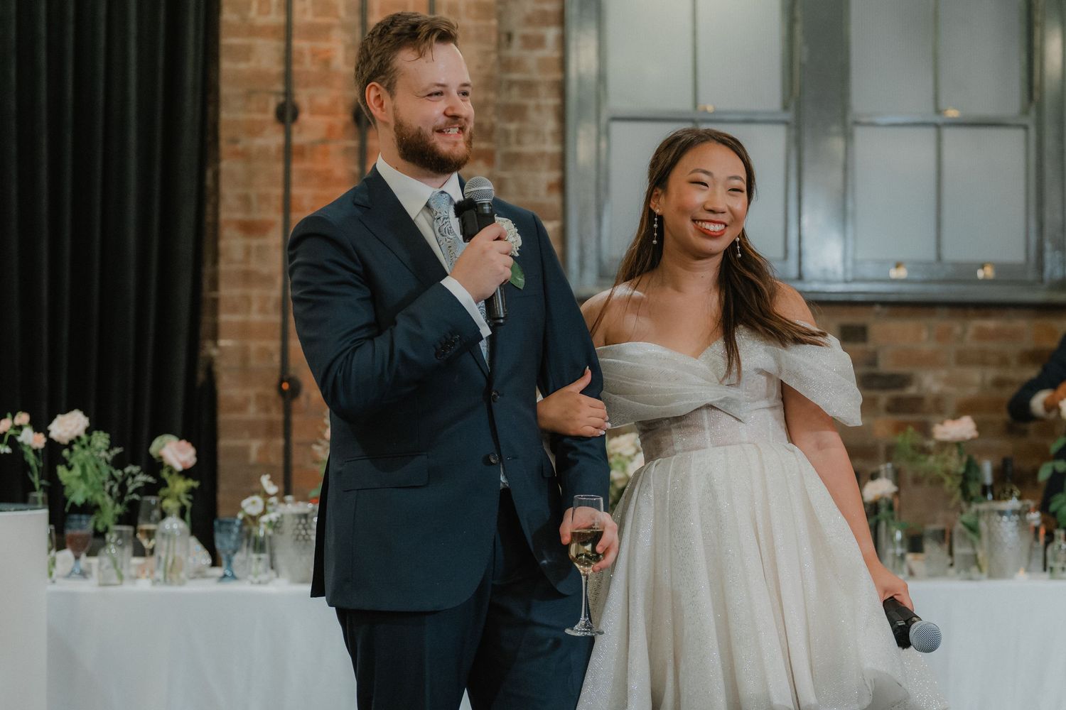 Couple shares a joyful moment during wedding speeches at an industrial venue.