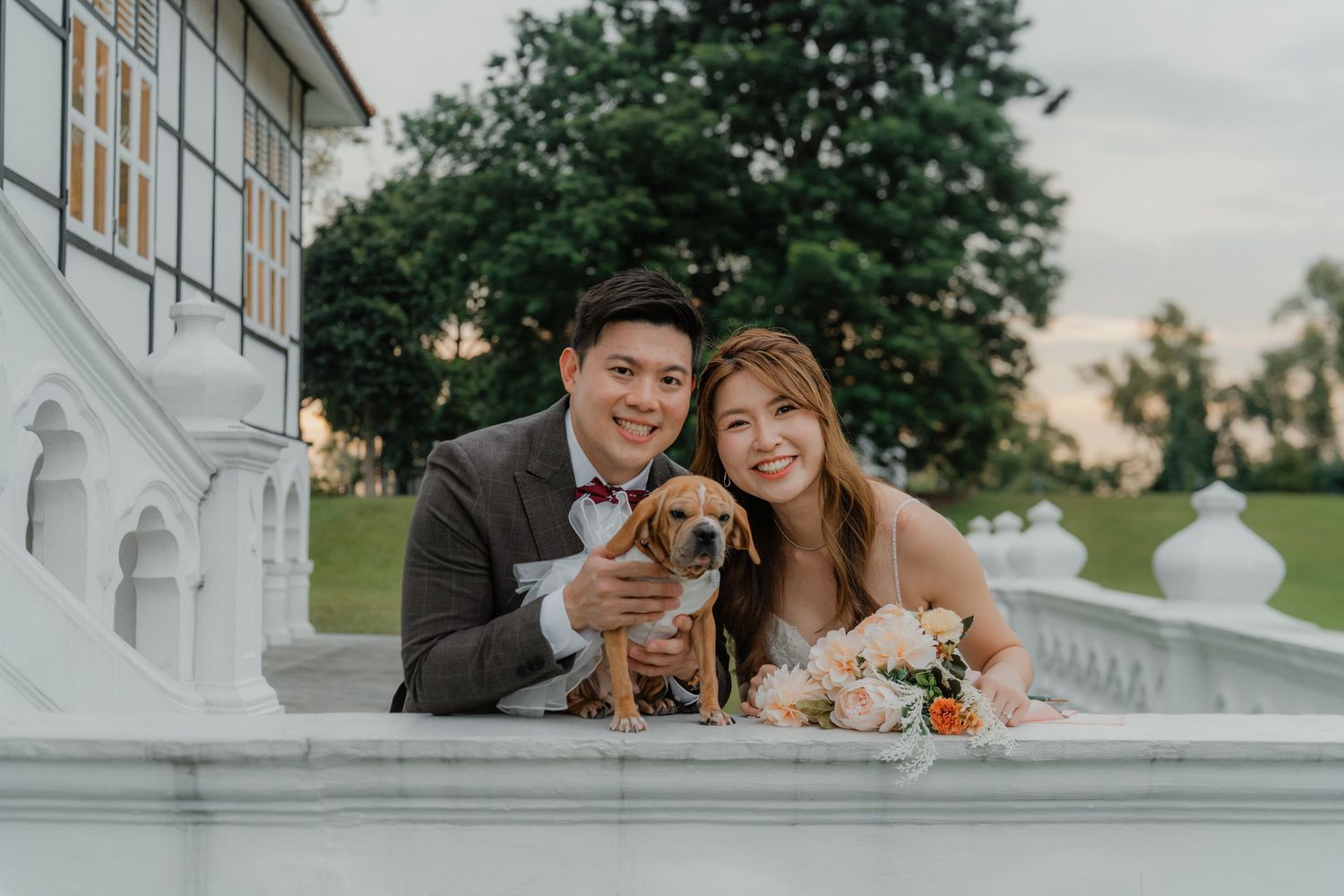 Happy couple in formal attire smiles together on elegant staircase with flowers during golden hour.