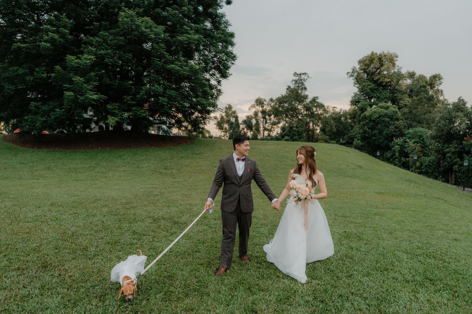 A couple walks together on a lush green hillside during their wedding celebration in an elegant outdoor setting.