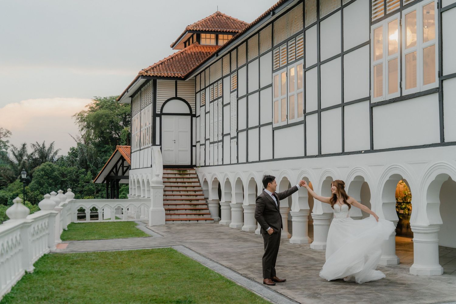 Wedding venue exterior featuring white arches and large windows at sunset.