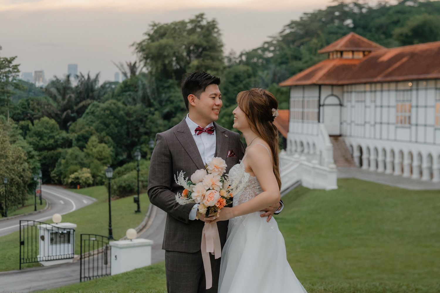 Newlywed couple celebrates their wedding day on a lush green lawn outside a beautiful white building.