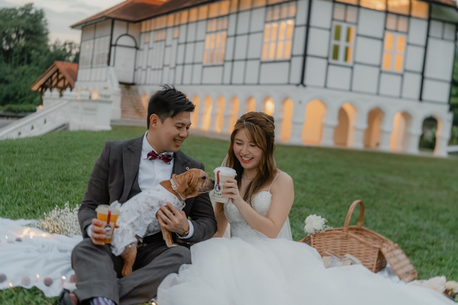 Couple enjoying drinks at an outdoor picnic with rustic building backdrop on a sunny afternoon.