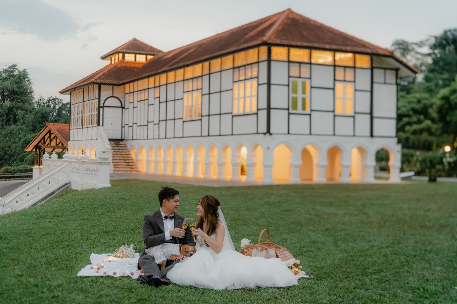 A wedding couple enjoys a sunset picnic in front of an elegant colonial-style building.