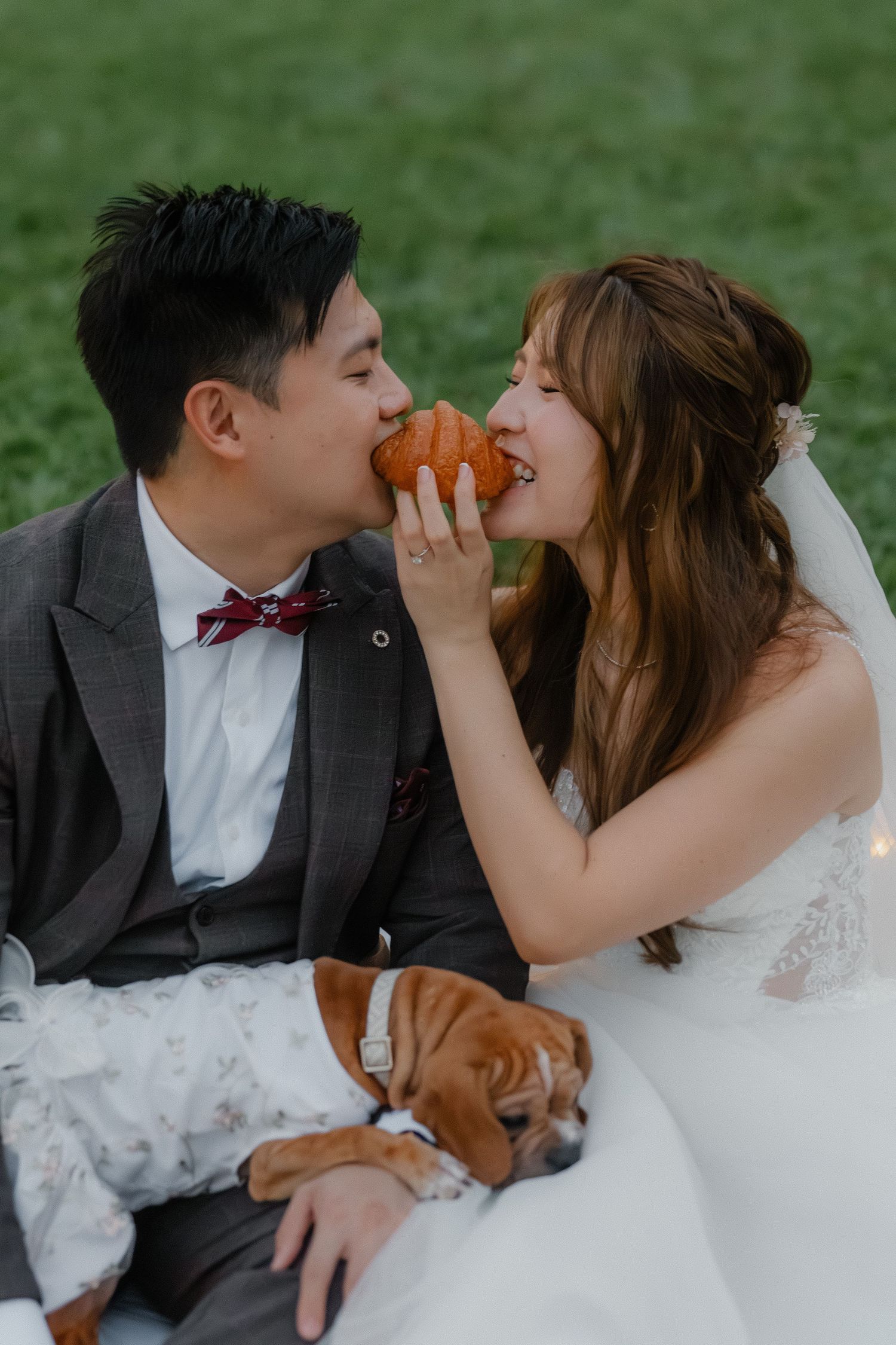 Couple shares a playful moment eating together on grass with their sleeping dog.