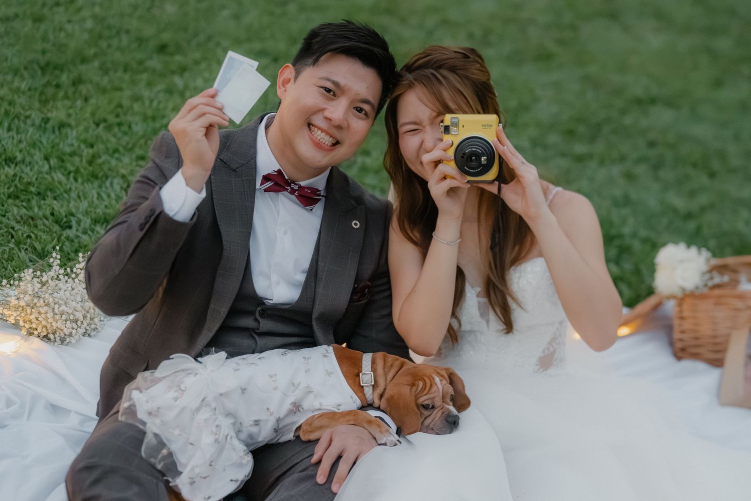 A couple poses playfully with drinks and a camera during their outdoor wedding photoshoot.
