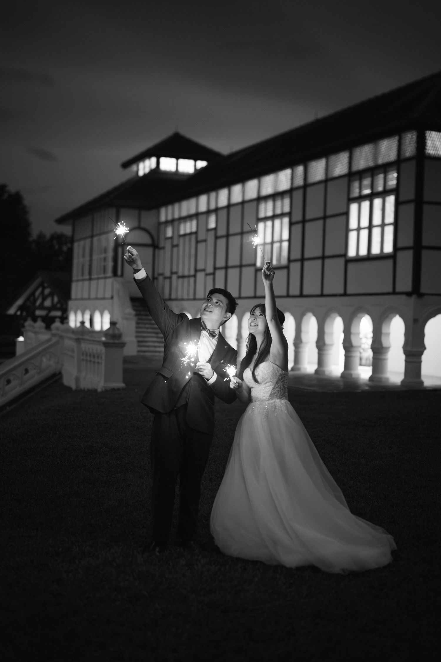 A romantic wedding scene at dusk with silhouettes dancing against illuminated windows of a large building.