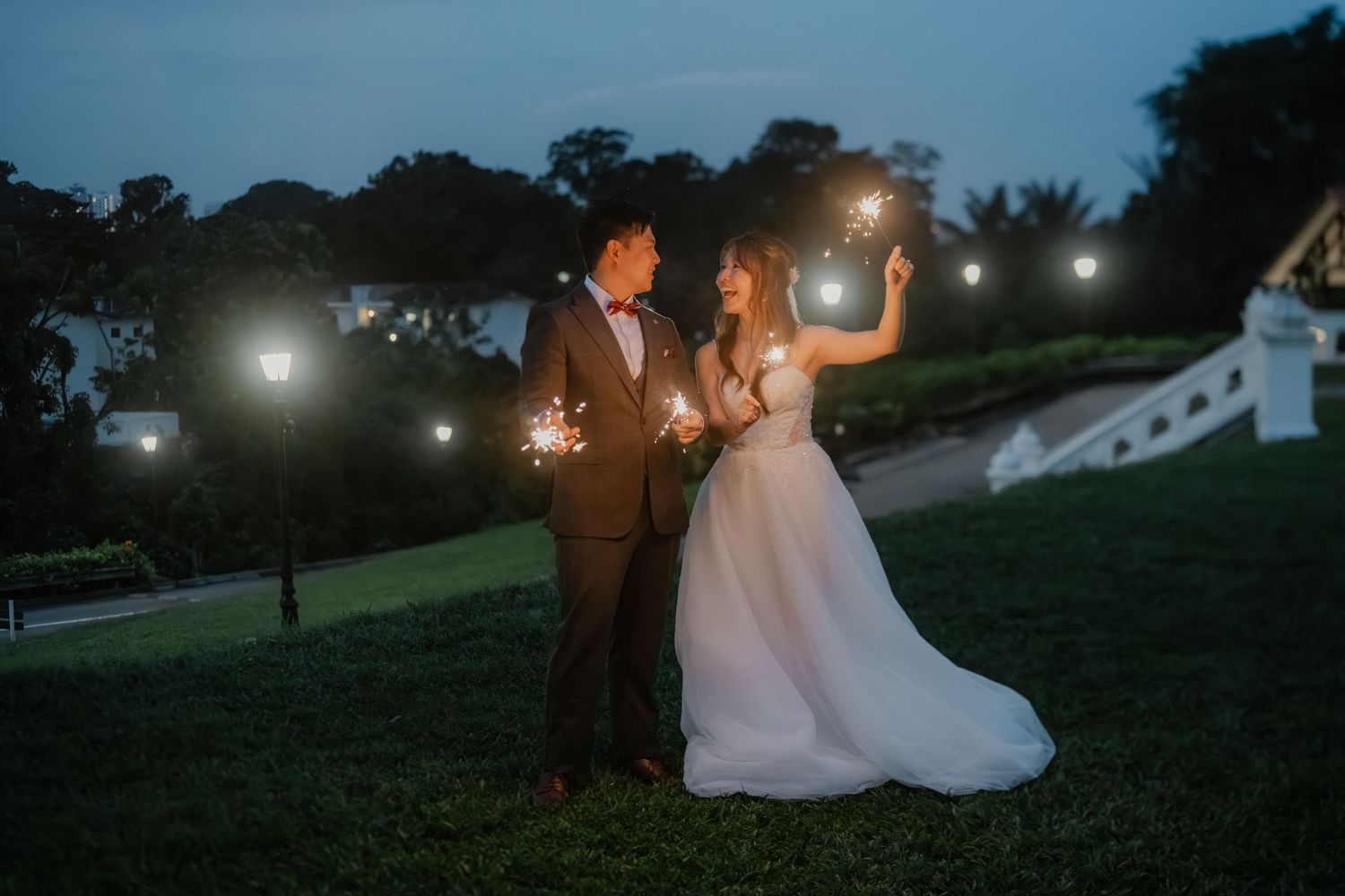 A couple holds sparklers while sitting on grass at dusk during a romantic outdoor celebration.