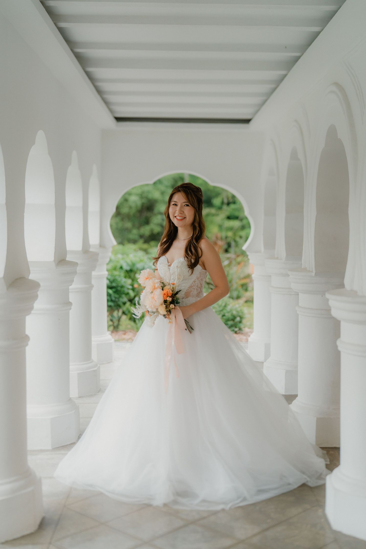 A flowing white wedding gown cascades between elegant white columns in an architectural setting.