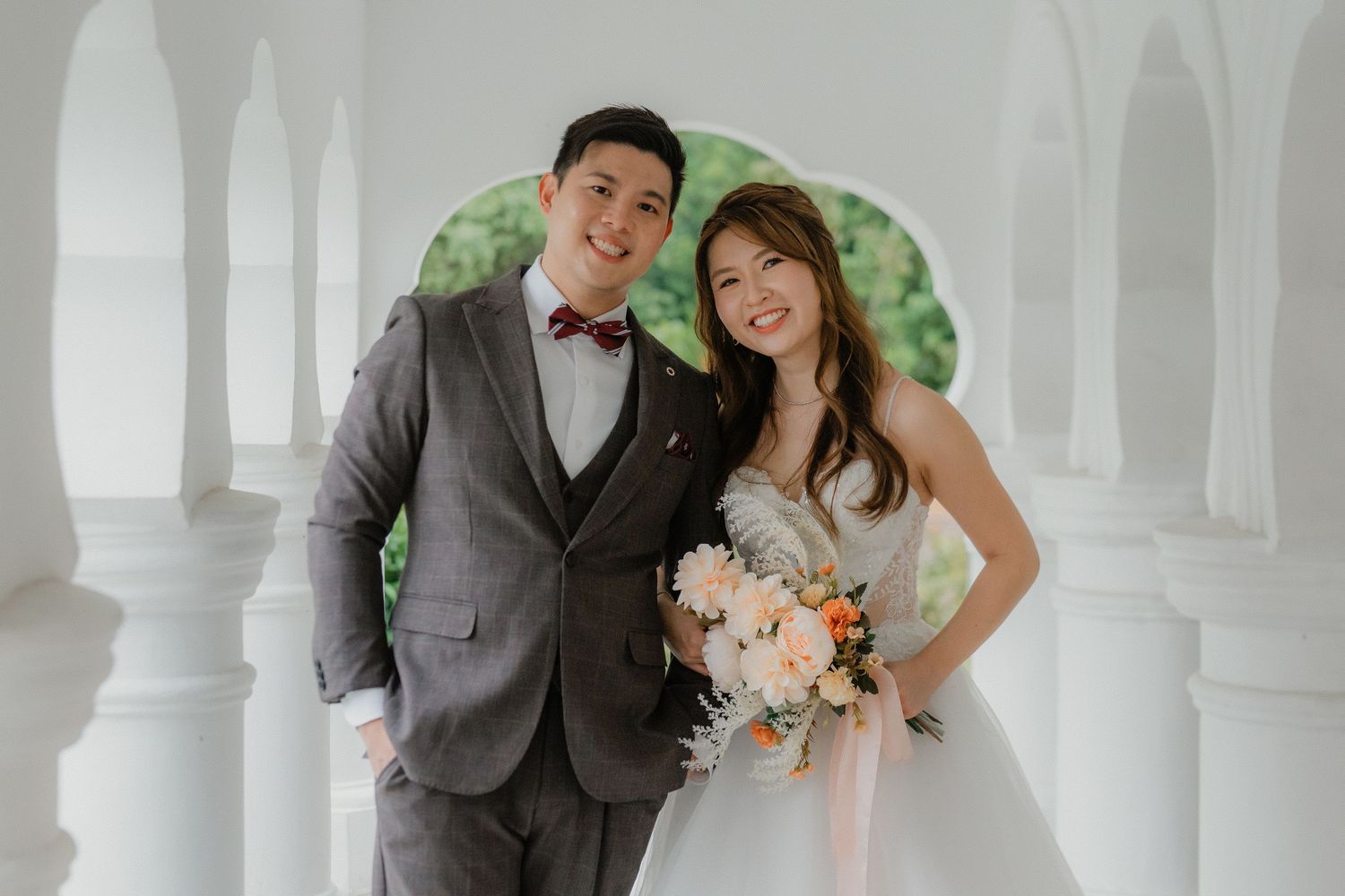 A couple poses together at their wedding with elegant arches and greenery in the background.