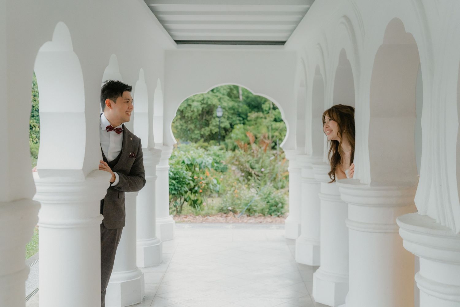 Couple walks together under elegant white arches on their wedding day against soft natural lighting.