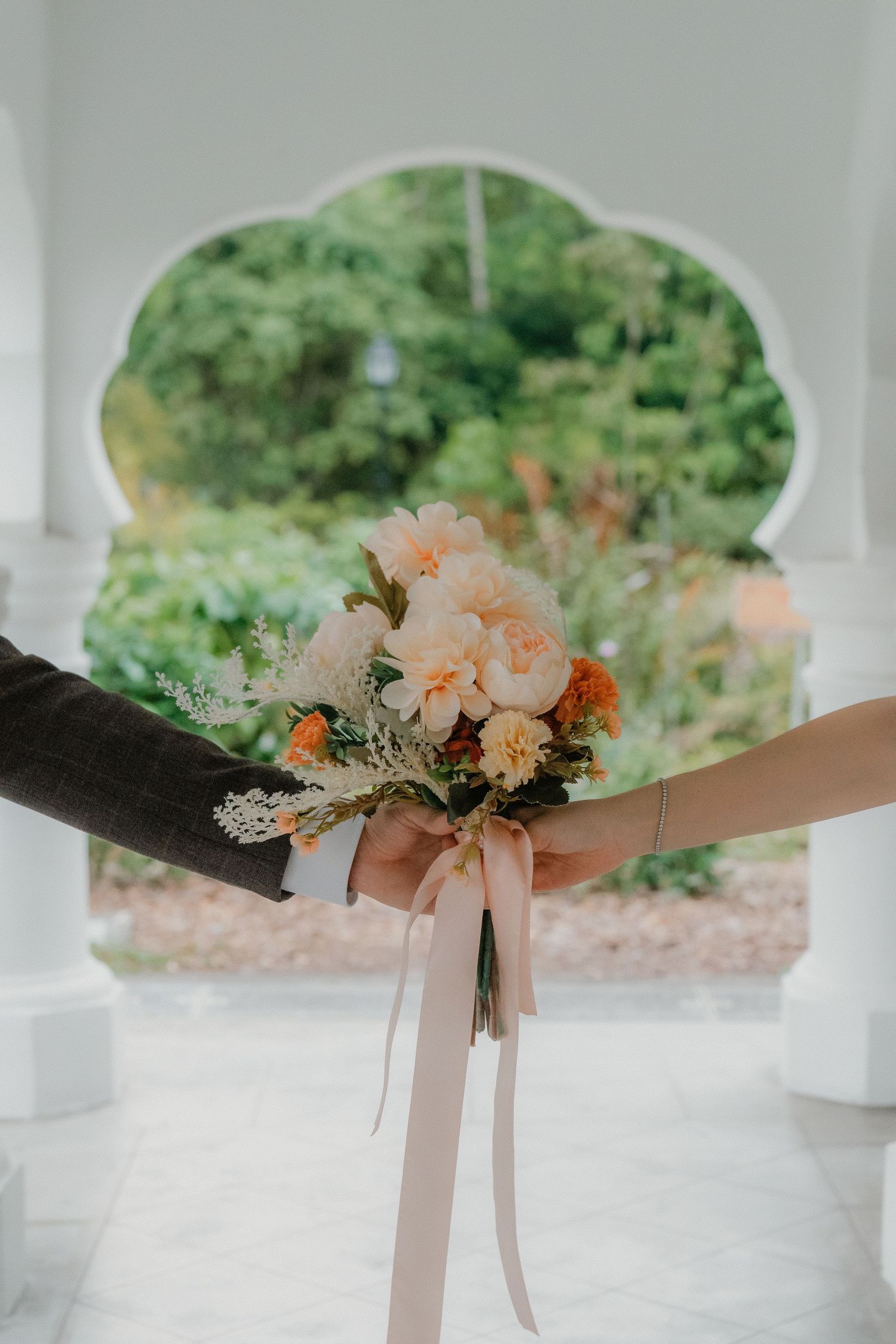 A series of soft peach and blush bouquets with silk ribbons displayed against a white background with greenery outdoors.