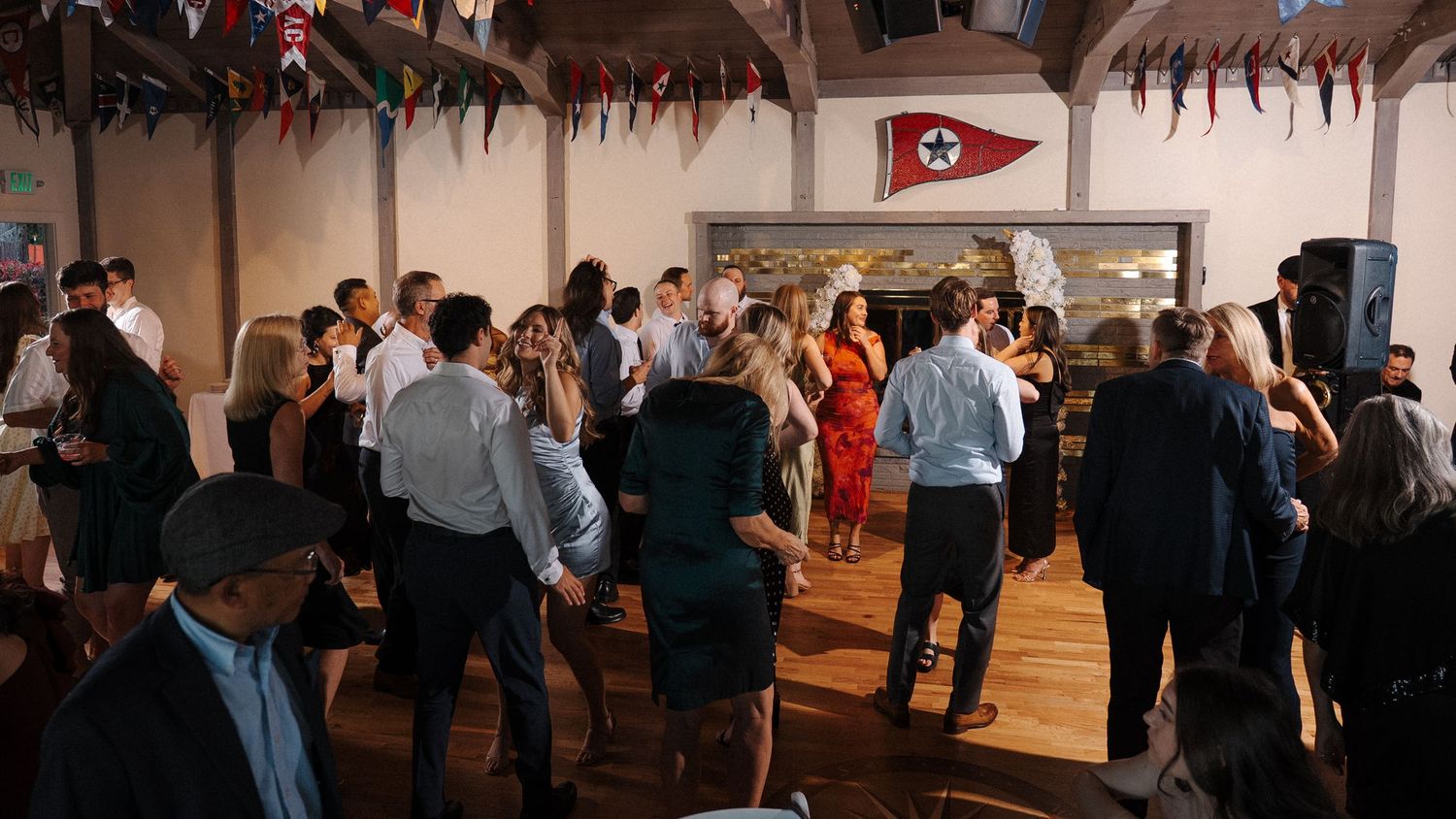 A panoramic view of people dancing in pairs during a social dance event in a spacious white-walled venue.