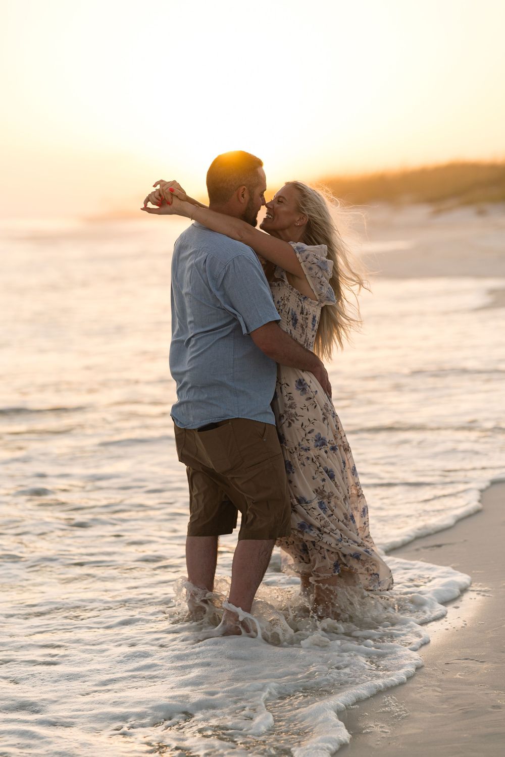 Romantic couple embracing and kissing on a sandy beach at sunset, waves washing over their feet.