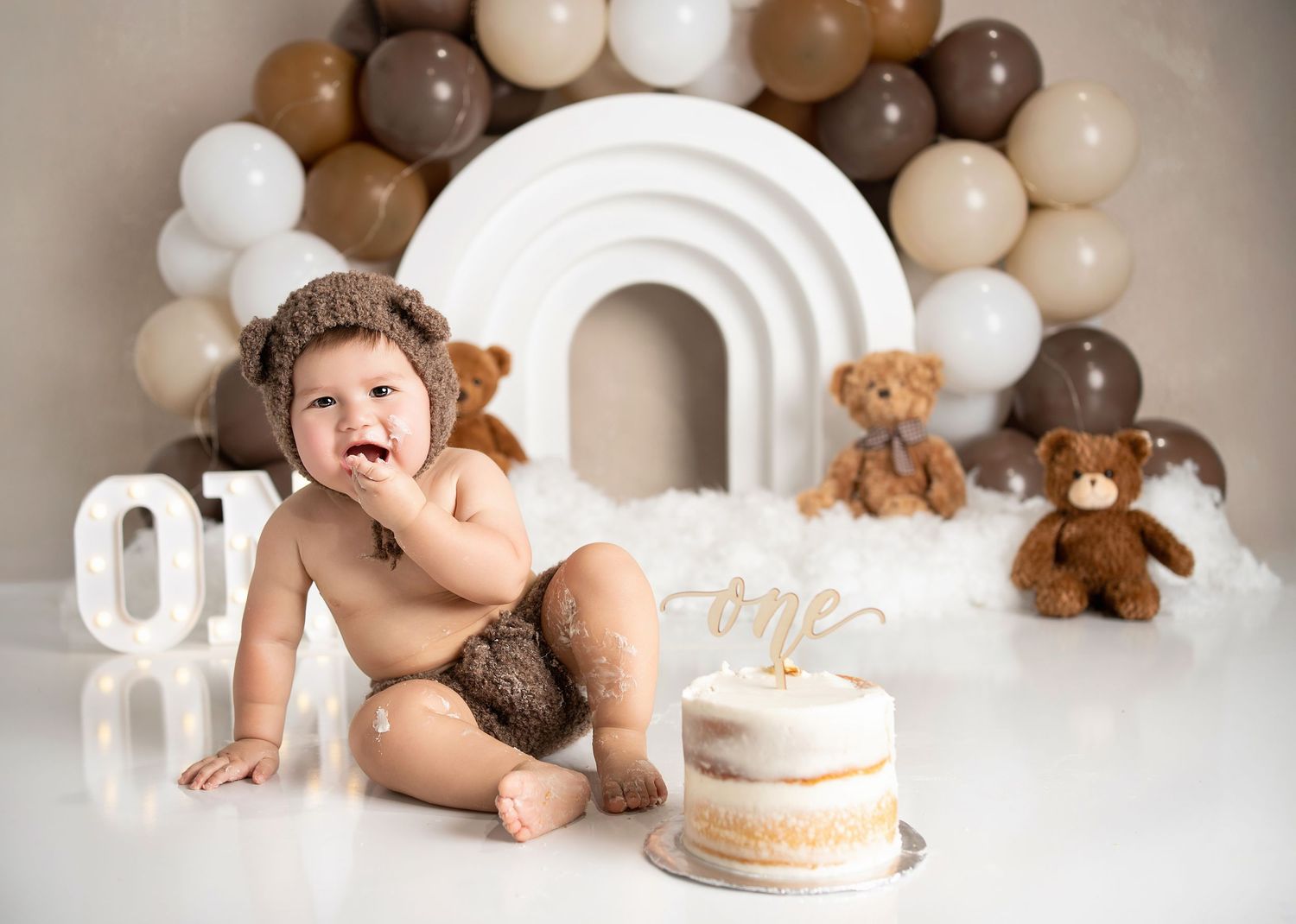 Baby with frosting on face during teddy bear-themed cake smash session.