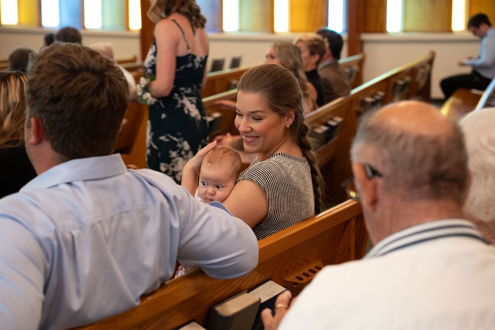 Guests at a wedding ceremony; a mother with her  baby on her lap.