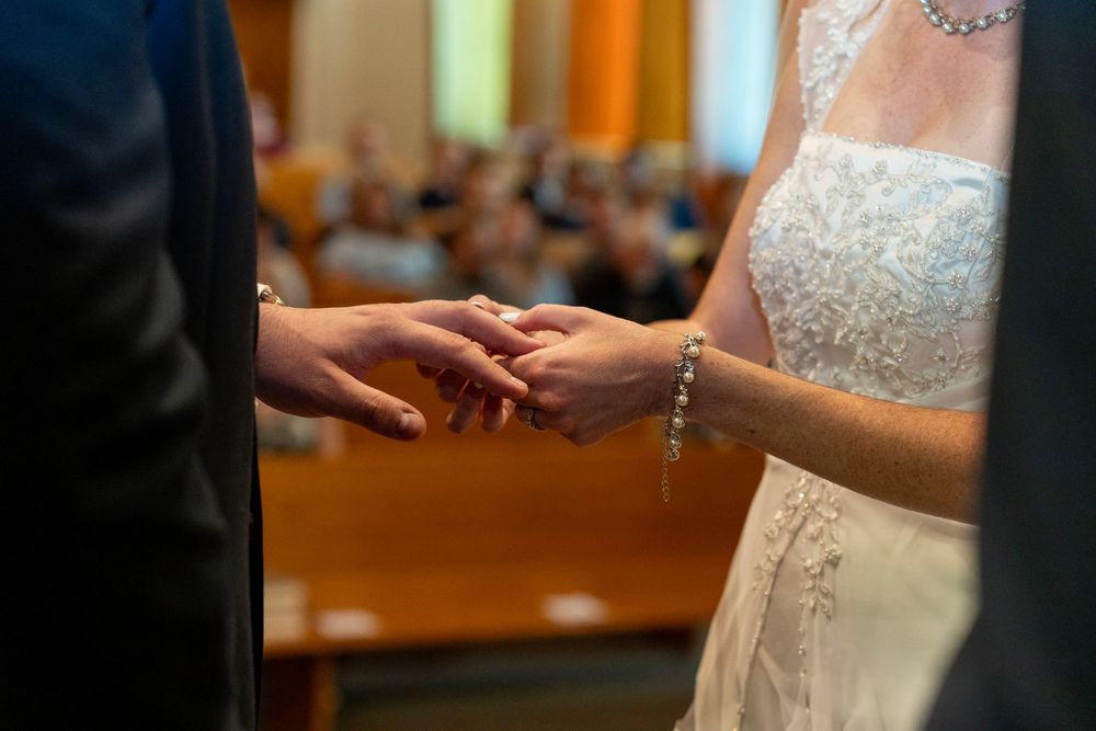 Ring ceremony at a wedding, with guests blurred in the background.