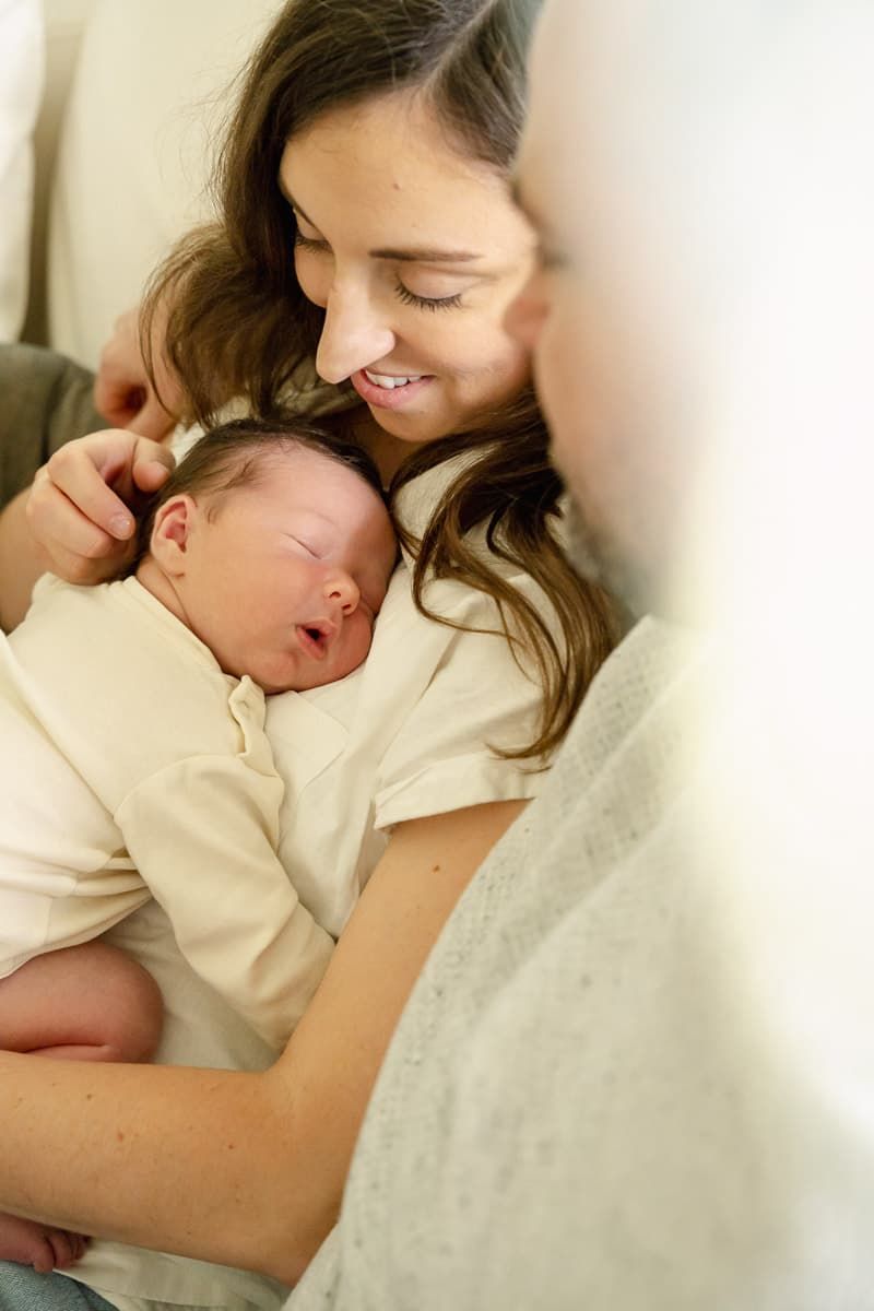 Mother in cream colored sweater lovingly holds sleeping newborn baby against her chest in tender moments during lifestyle session.
