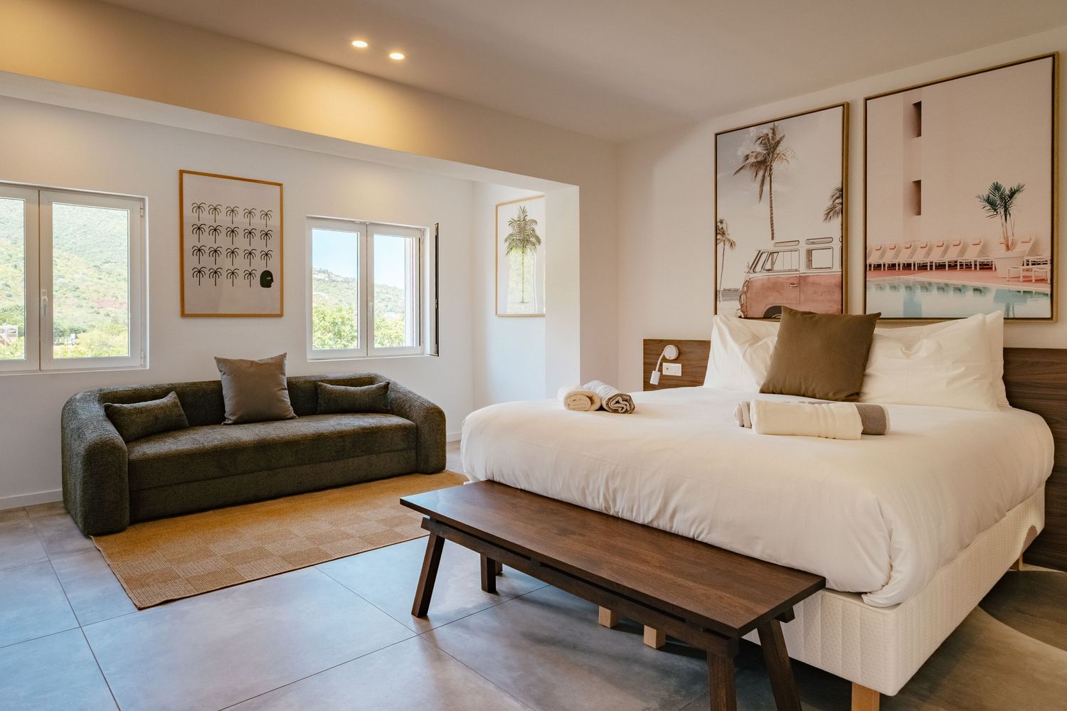 Modern hotel room interior with dark green sofa, white bed, wooden bench and minimalist wall art decor.