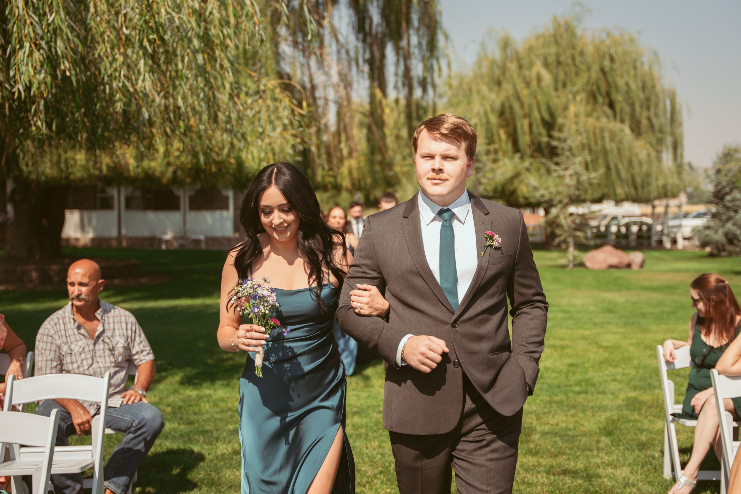 A line of wedding guests walking across bright green grass during an outdoor summer celebration.
