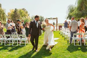 Wedding guests gather on a beautiful lawn with white chairs during an outdoor ceremony.