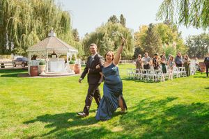 Scenic outdoor wedding venue with weeping willows and white chairs arranged on green grass.
