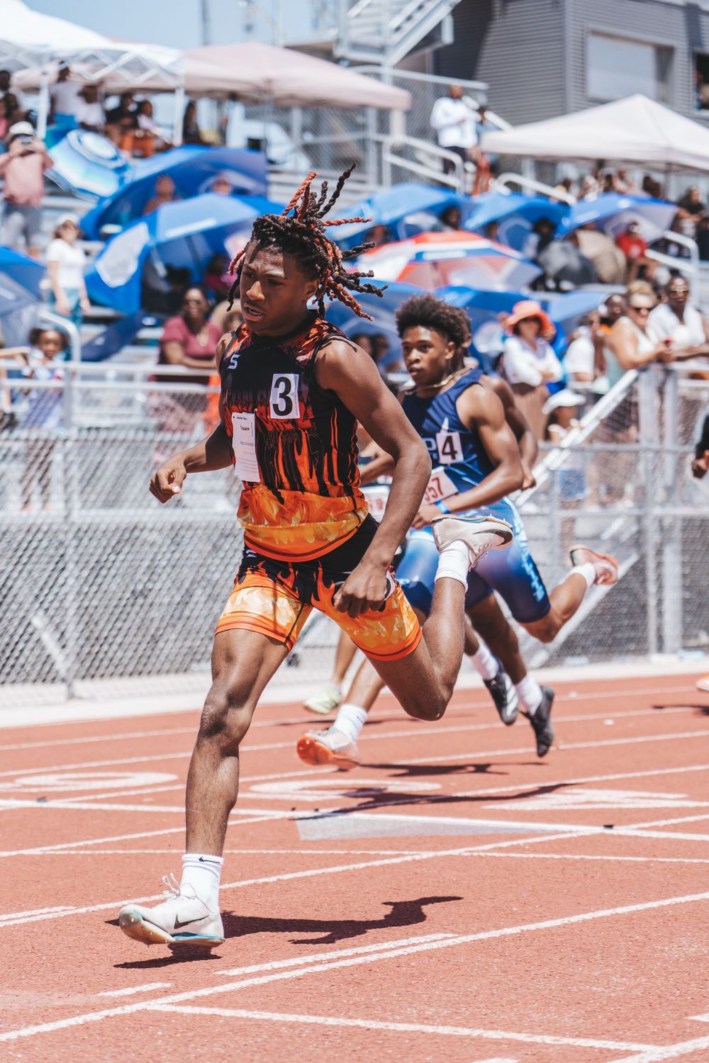 Runner in orange uniform competing in track event with spectators in background.