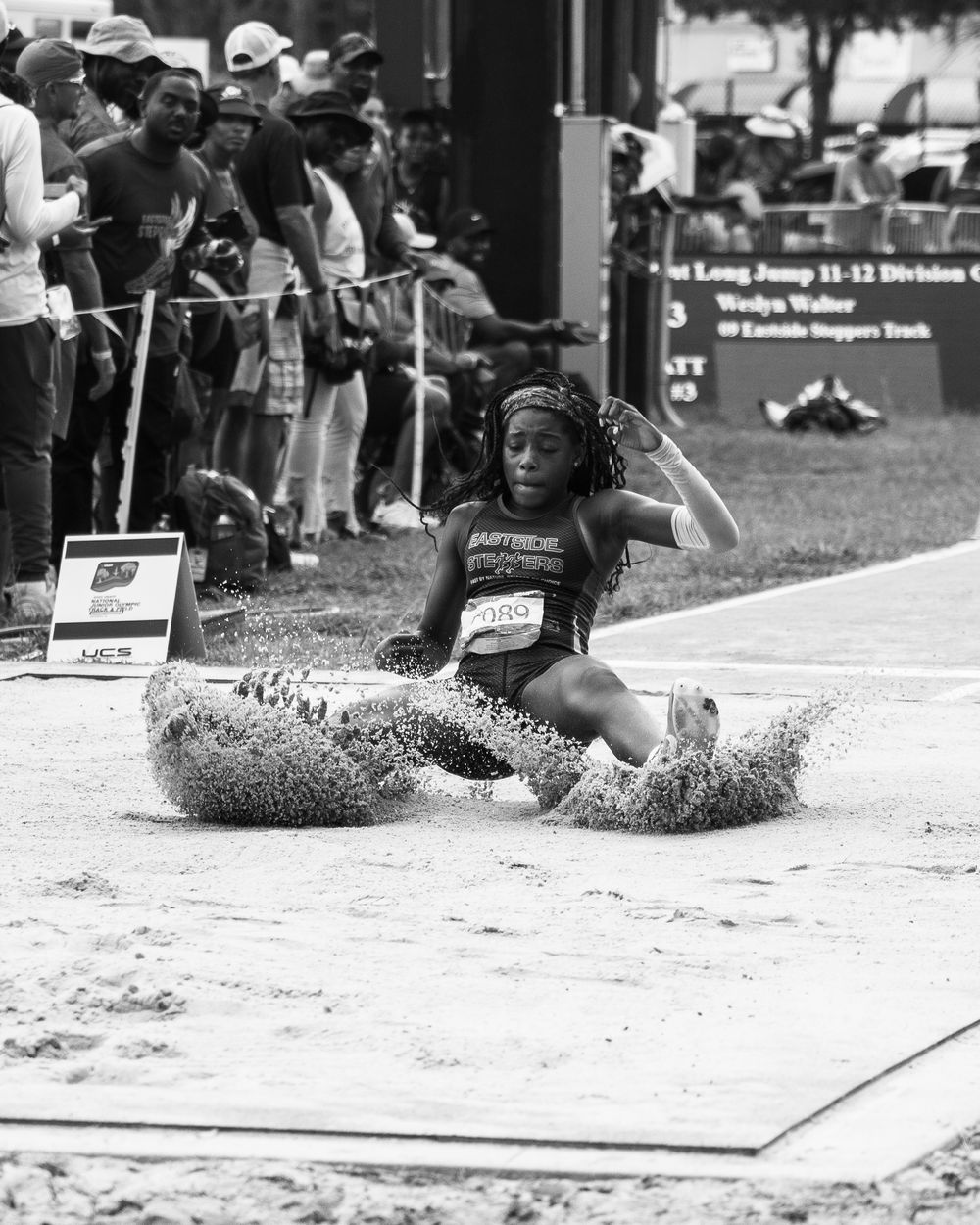 Track athlete performs long jump landing in sand pit during competition.