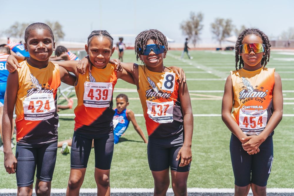 Group of young athletes in racing uniforms standing together on track field.