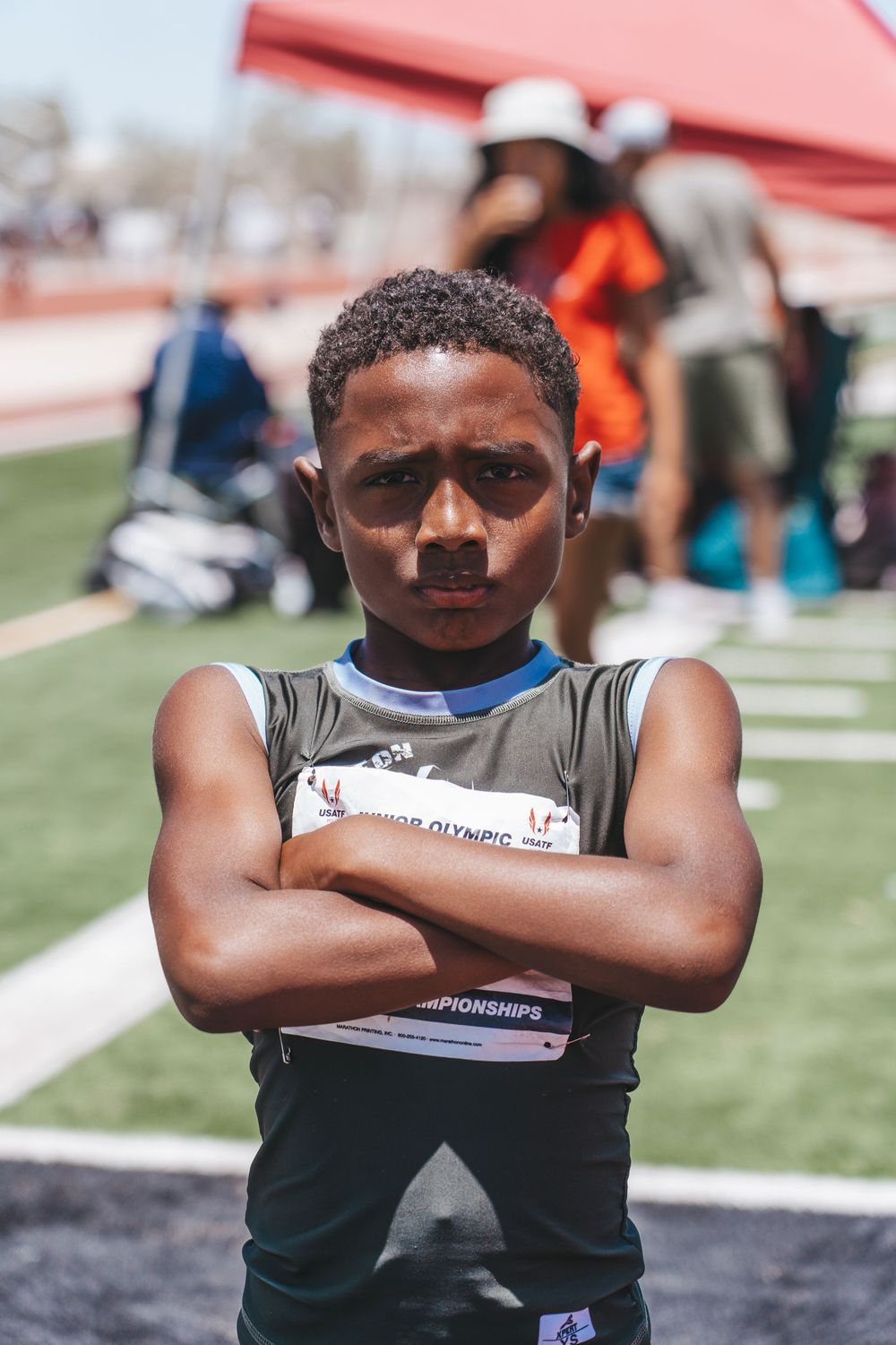 Young athlete in athletic uniform standing with crossed arms on field.