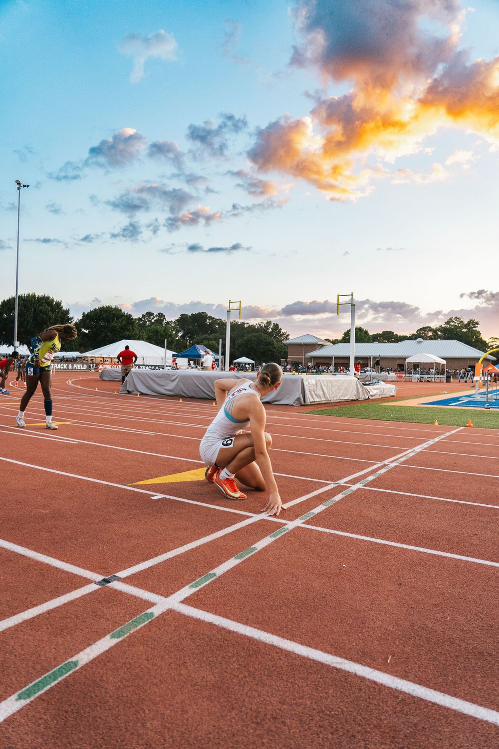 Athlete crouching at finish line during sunset track meet.