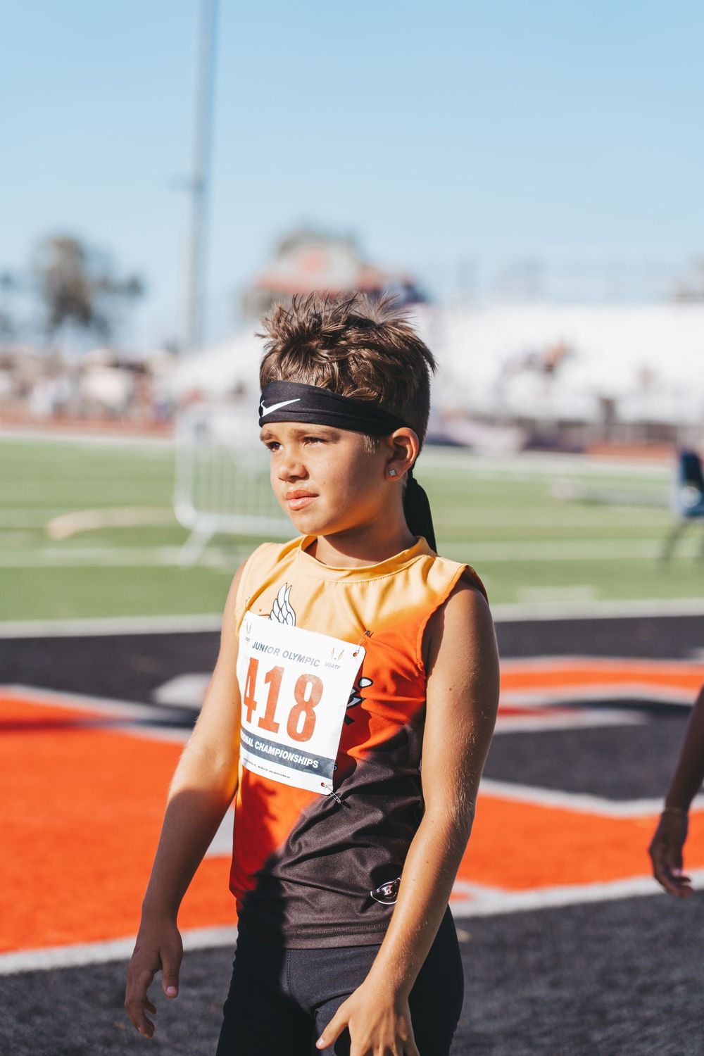 Athletes in orange and black uniforms prepare for race at outdoor track.