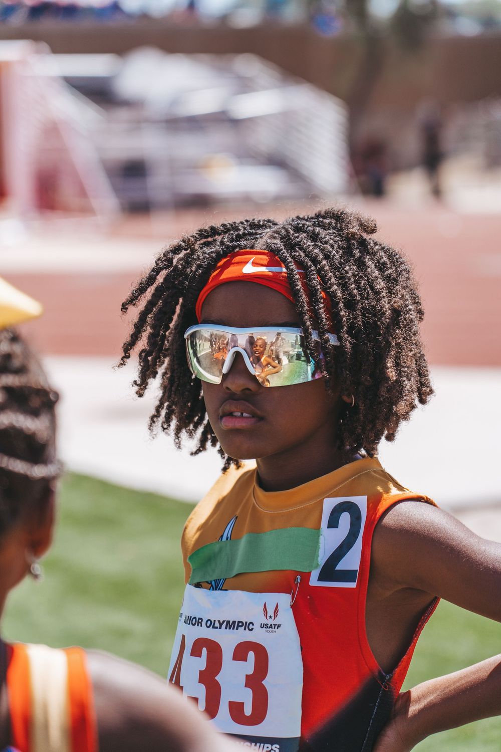 Track athlete wearing sunglasses and orange racing bib number 433 at outdoor competition.