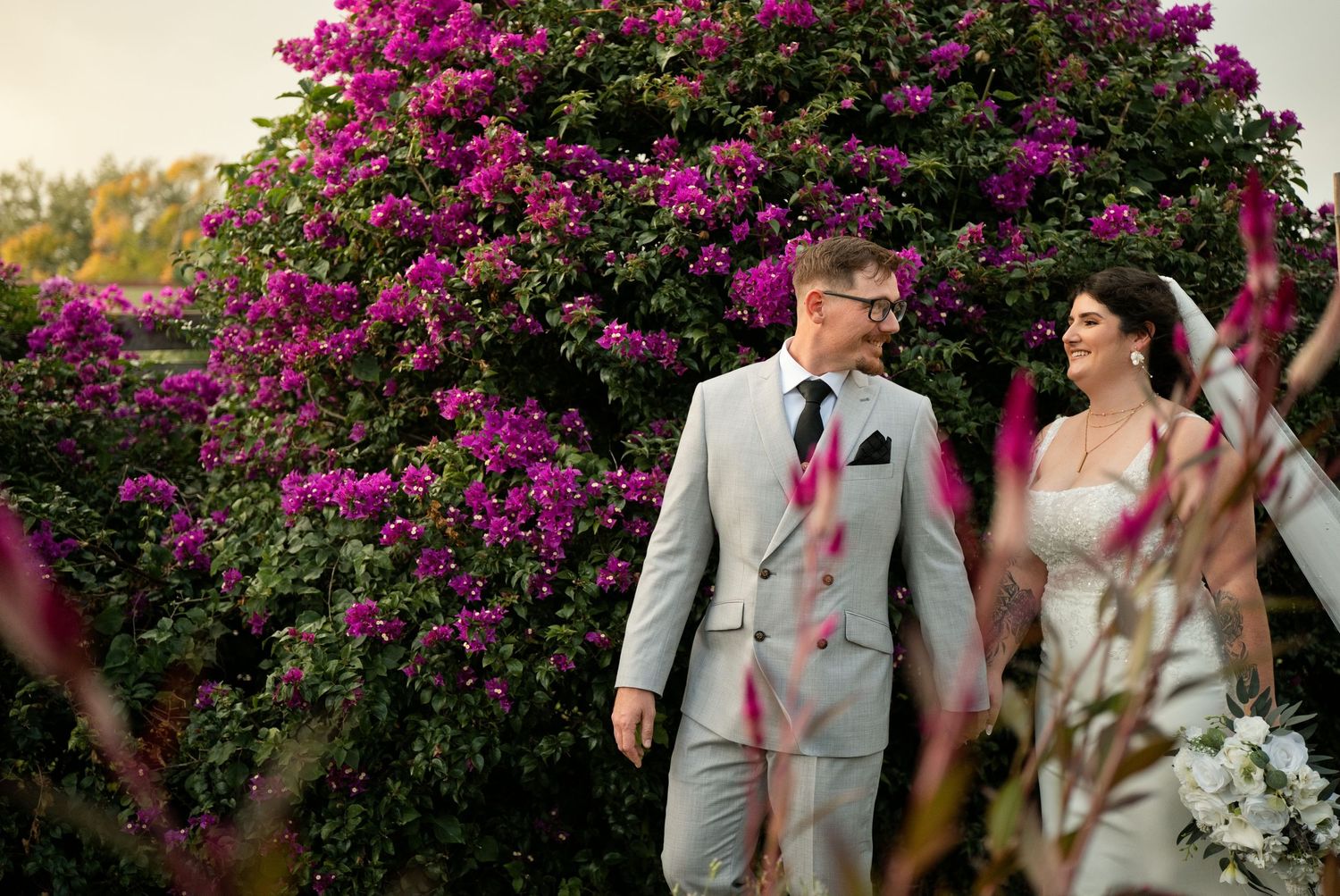 Bride and groom walking together in front of vibrant pink bougainvillea flowers on their wedding day. The Acre wedding venue, Orlando.