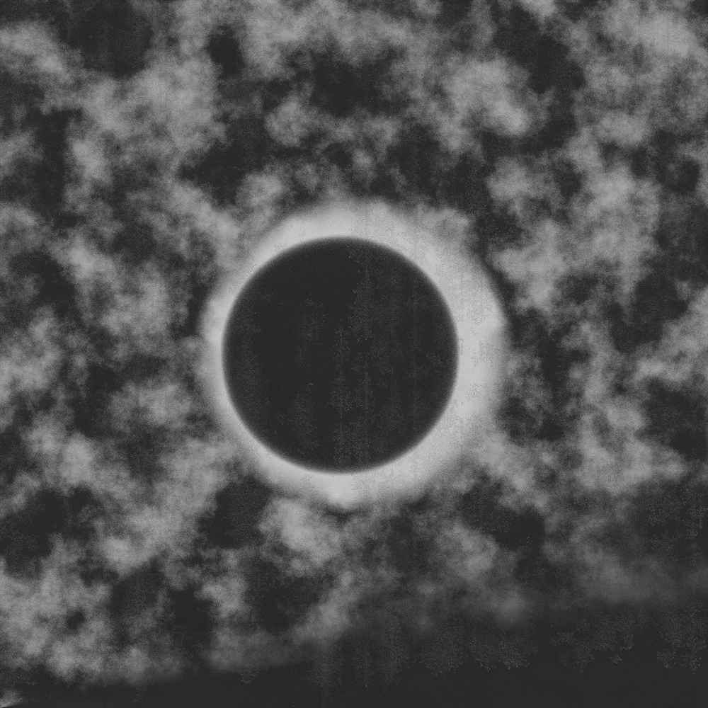 A striking black and white photograph of a total solar eclipse with a bright corona visible through wispy clouds.
