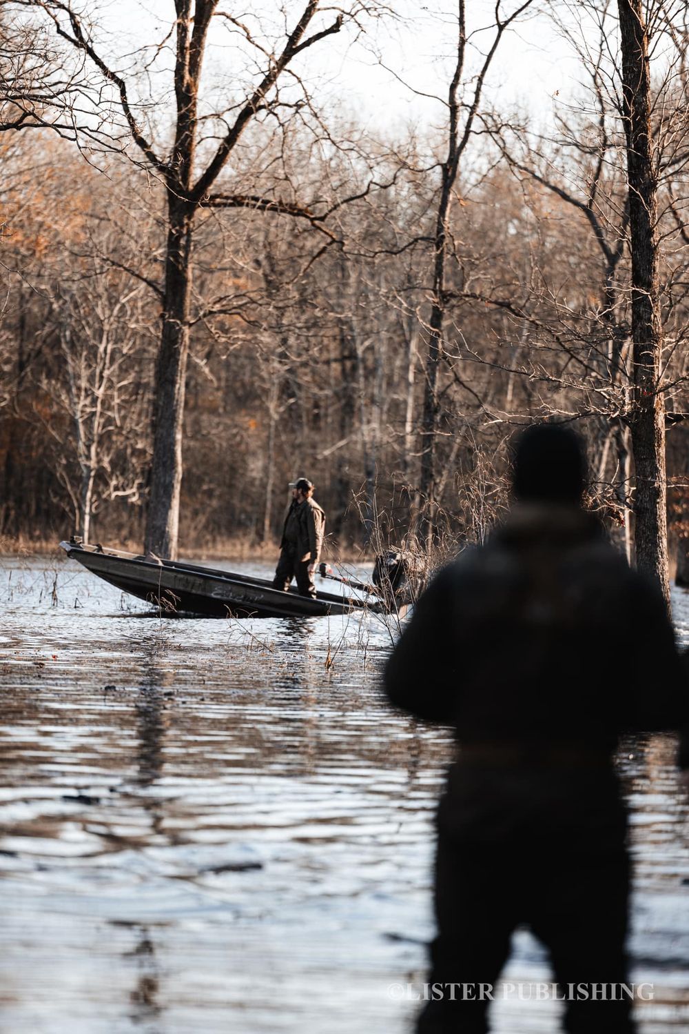 Silhouetted hunters on a small boat in flooded winter woods.