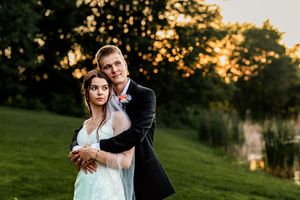A romantic couple embraces on a grassy hillside during golden hour sunset.