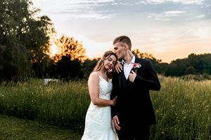 A beautiful sunset wedding photo shows a romantic moment between a couple in a grassy meadow field at dusk.
