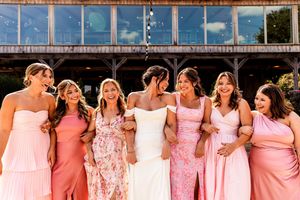 Happy bridal party wearing pink and coral dresses standing together at outdoor venue.