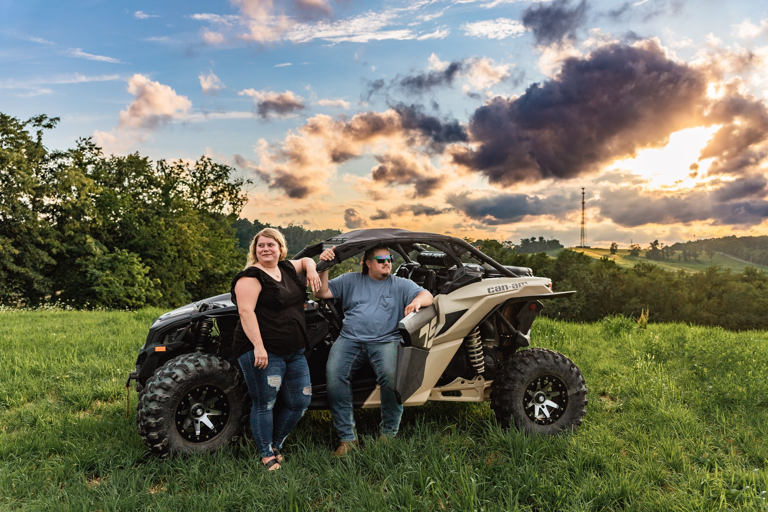 An ATV is parked in a grassy field during sunset with dramatic clouds in the sky and rolling hills in the background.
