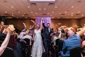Newlyweds joyfully walk through a crowd of celebration with raised hands at their wedding reception.