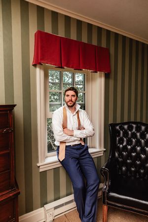 Professional photography of someone in business attire sitting on a leather chair against striped wall decor.