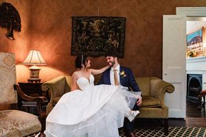 Bride and groom share an intimate moment on vintage furniture in a warmly lit room with terracotta walls.
