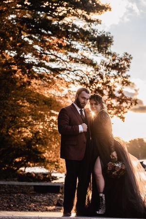 A romantic sunset wedding photoshoot with warm autumnal lighting filtering through the trees in the background.
