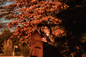 A person in a brown coat stands among vibrant orange autumn foliage during golden hour lighting.