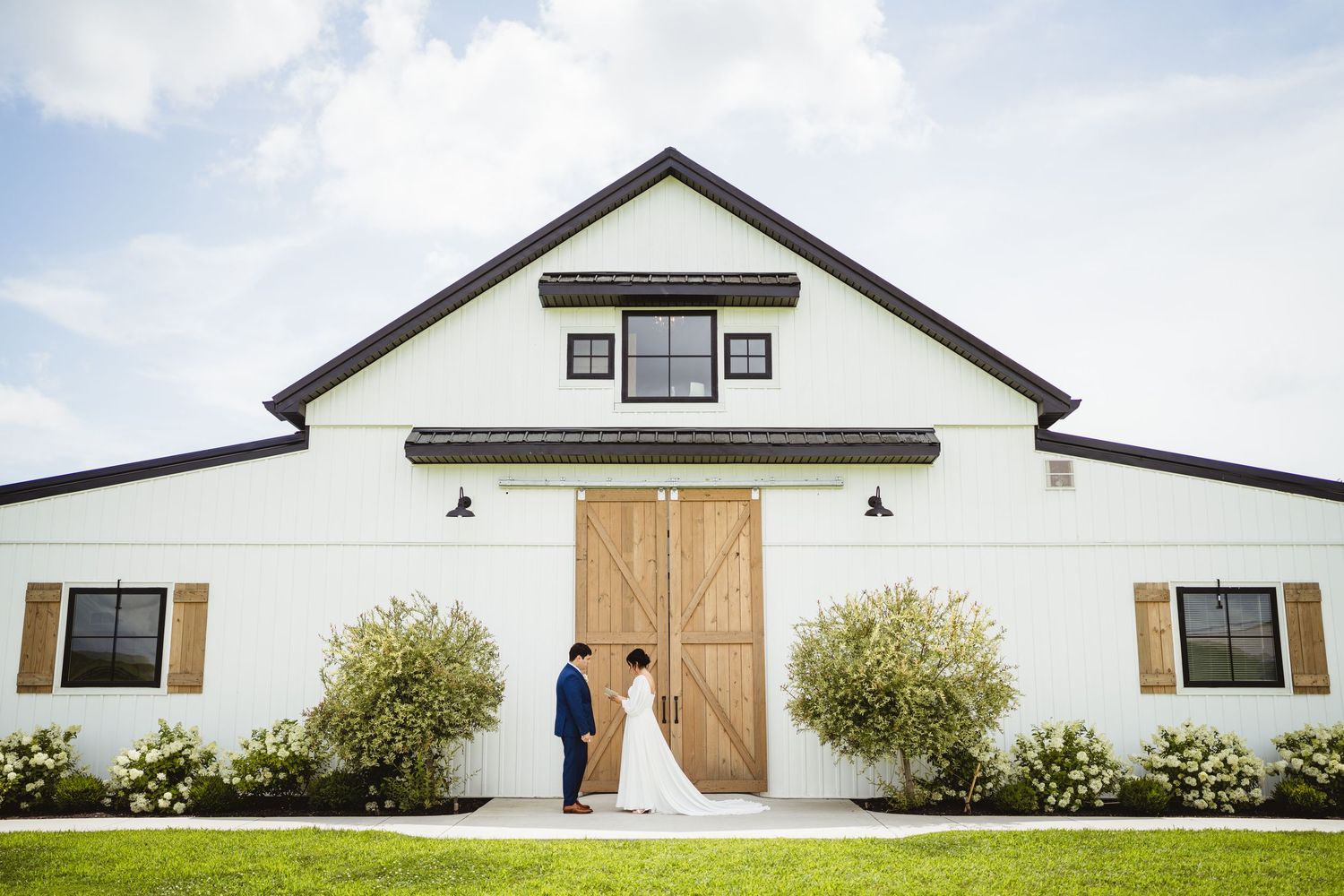 Modern white farmhouse style building exterior with large wooden door and minimal architectural details.