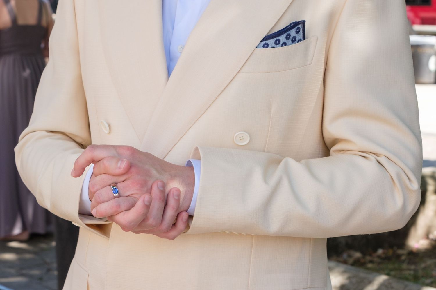 Person wearing a cream double-breasted suit jacket with a blue patterned pocket square, adjusting their watch.