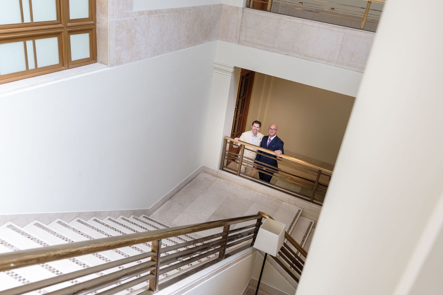 Modern white staircase with wooden handrail and metal railings leads up multiple floors in a commercial building.