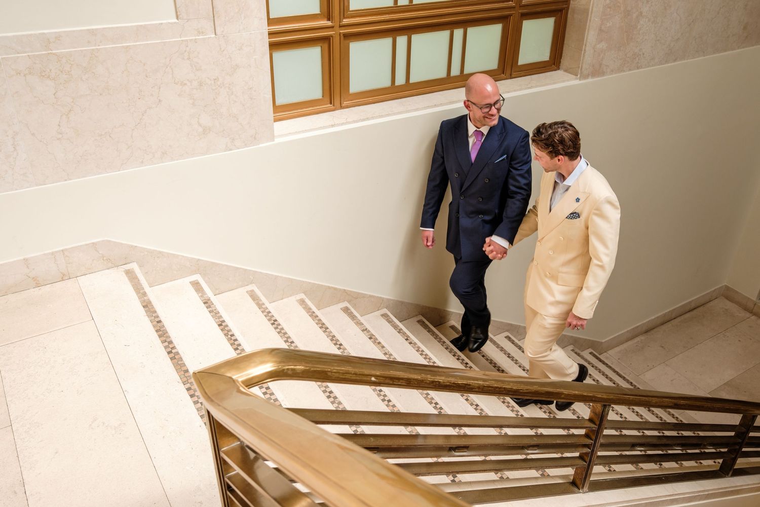 Two people in formal attire walking down an elegant marble staircase in a modern building interior.